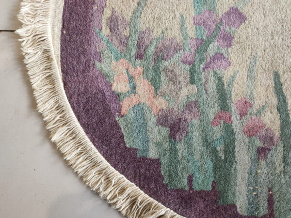 Round high-pile rug detail shows purple, green, and pink flowers, cream fringe, and light tiled flooring.
