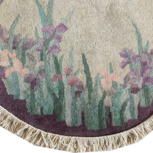Cream round rug corner with a purple border and fringe, patterned with pink and teal flowers.