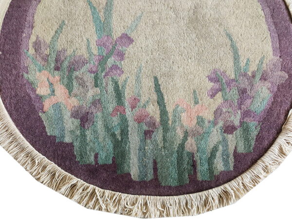 Cream round rug corner with a purple border and fringe, patterned with pink and teal flowers.