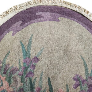 Beige, purple, pink, and teal round rug detail showing a floral pattern and short, fringed edge.
