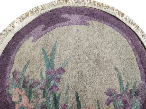 Beige, purple, pink, and teal round rug detail showing a floral pattern and short, fringed edge.