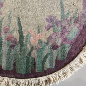 Close-up of a high-pile round rug with cream fringe and purple, pink, and green floral design.