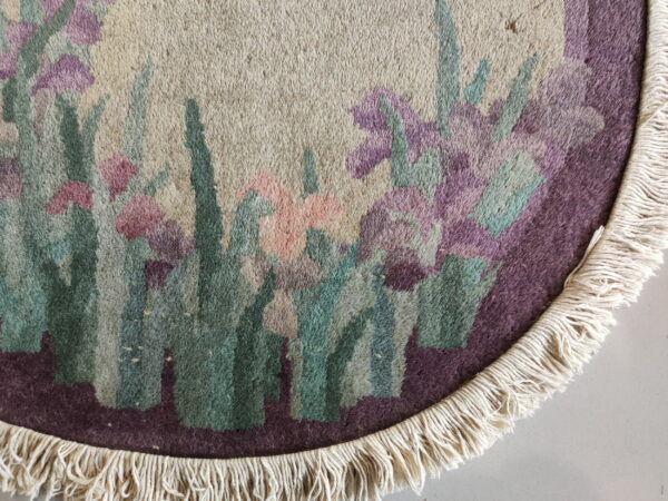 Close-up of a high-pile round rug with cream fringe and purple, pink, and green floral design.