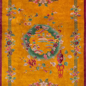 Plush gold rug with a magenta border, teal geometric trim, and scattered pink and green floral designs.