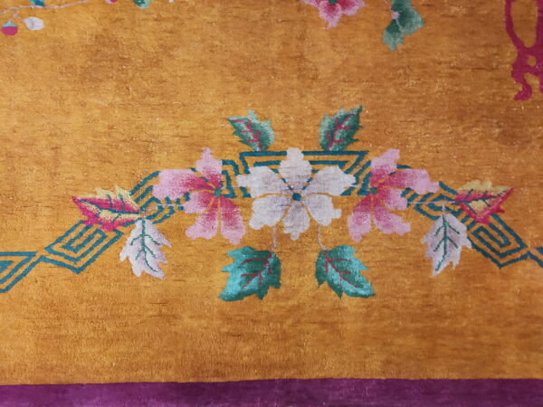 Golden high-pile rug detail featuring pink and white flowers, teal leaves, and a purple border.