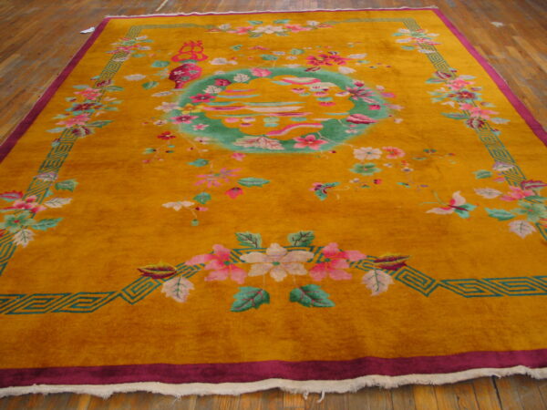 Yellow rug with large pink and green floral designs, a teal medallion, and magenta borders on wood planks.