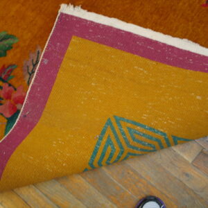 Orange high-pile rug flipped on wood floor, showing yellow and magenta backing with a teal geometric pattern.
