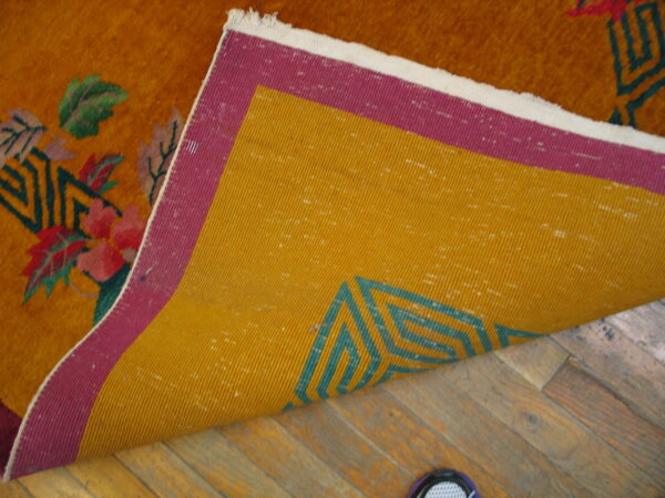 Orange high-pile rug flipped on wood floor, showing yellow and magenta backing with a teal geometric pattern.