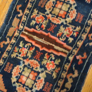 Ornate navy blue rug featuring coral, tan, and brown accents on a natural hardwood floor.