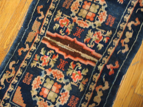 Ornate navy blue rug featuring coral, tan, and brown accents on a natural hardwood floor.
