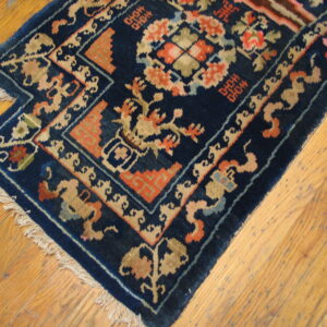A dark navy blue traditional rug with coral and tan patterns rests on distressed wooden floorboards.