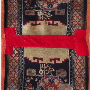 Worn dark rug with red, gold, and blue patterns, visible patches, and a bright red horizontal fabric strip.