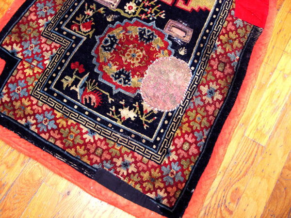 Low-pile dark blue rug with red, gold, and light blue traditional motifs, exposed edges, on wood planks.