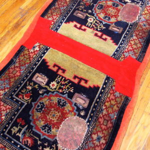 Dark blue patterned runner rug with red and yellow designs, showing extensive repairs on wood floor.