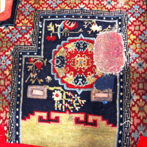 Low-pile rug fragment in navy, red, and gold, showing complex patterns, wear, and a bright pink patch.
