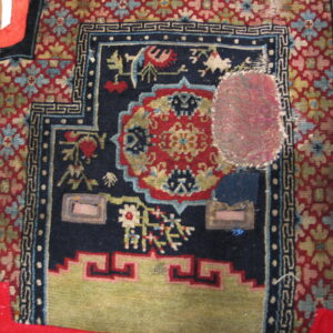 Detailed view of a worn navy, red, and green patterned rug with a visible oval pink fabric patch.