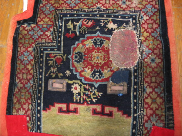 Detailed view of a worn navy, red, and green patterned rug with a visible oval pink fabric patch.