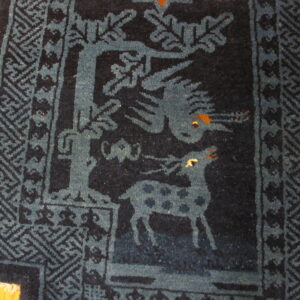 Close-up of a dark indigo rug featuring blue animal motifs and a patterned geometric border on wood flooring.