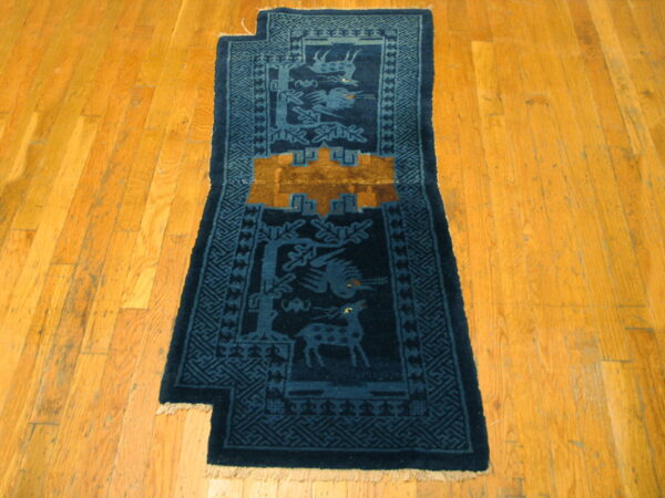 Dark blue animal motif runner with gold details and a notched edge lies on diagonal wood flooring.