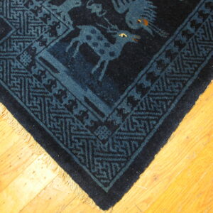 Dark blue rug corner with animal figures and geometric borders rests on bright wooden floorboards.