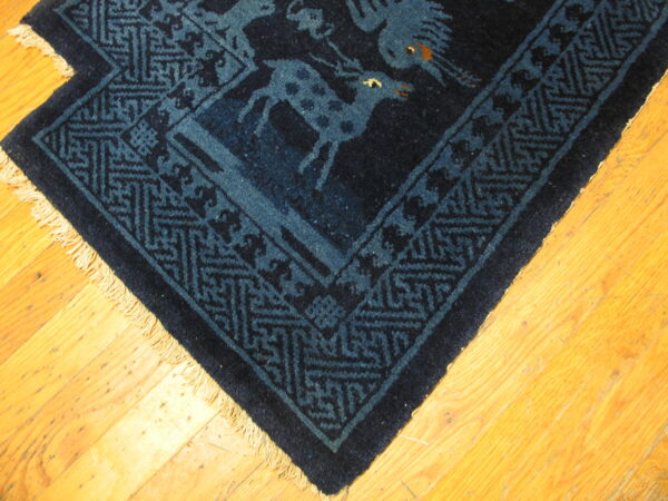 Dark blue rug corner with animal figures and geometric borders rests on bright wooden floorboards.