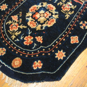 Curved navy area rug with coral, gold, and light blue floral patterns lies on bright wood planks.