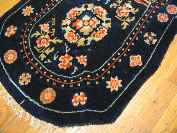 Curved navy area rug with coral, gold, and light blue floral patterns lies on bright wood planks.