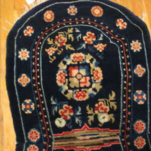 A navy blue arched rug featuring intricate red, cream, and olive floral motifs rests on light wood flooring.
