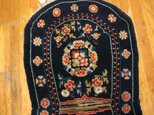 A navy blue arched rug featuring intricate red, cream, and olive floral motifs rests on light wood flooring.