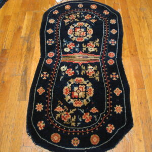 Small dark blue rug featuring red and tan floral motifs rests on worn light brown hardwood planks.