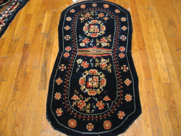Small dark blue rug featuring red and tan floral motifs rests on worn light brown hardwood planks.