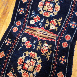 Dark blue runner rug with red and cream floral and geometric patterns lies on a distressed wood floor.