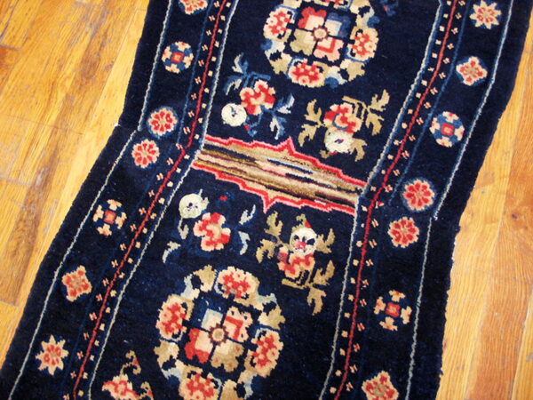 Dark blue runner rug with red and cream floral and geometric patterns lies on a distressed wood floor.