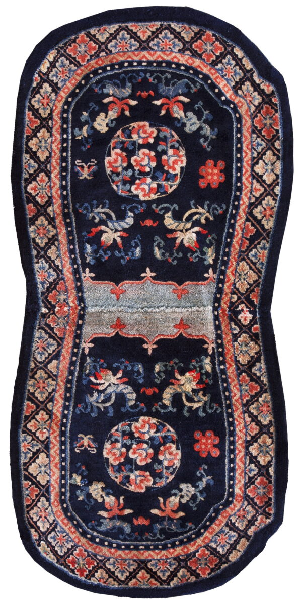 A navy blue saddle-shaped rug featuring stylized red, blue, and tan floral motifs and borders.