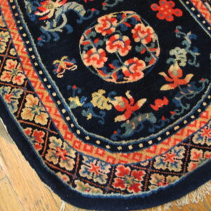 Dark blue rug with red and beige floral and figure motifs, rounded edge, bordered, lying on wood floor.