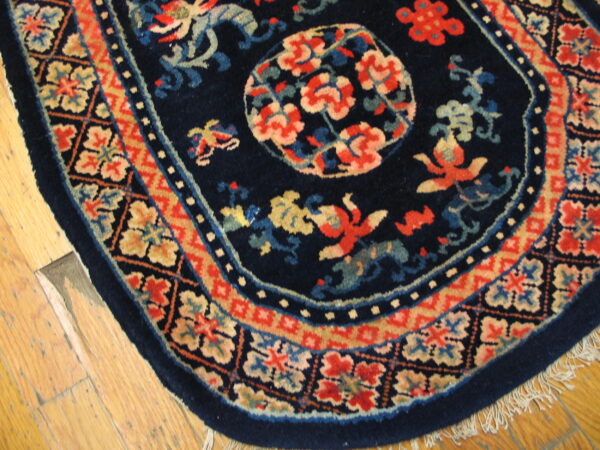 Dark blue rug with red and beige floral and figure motifs, rounded edge, bordered, lying on wood floor.