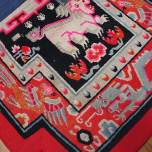 Figural rug with bright pink, red, black, cream, and blue designs lies over wood flooring.