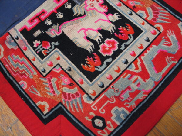 Figural rug with bright pink, red, black, cream, and blue designs lies over wood flooring.