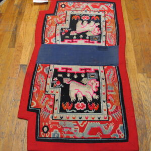Red and black patterned textile with light mythical animals and a central blue band, displayed on wood floors.