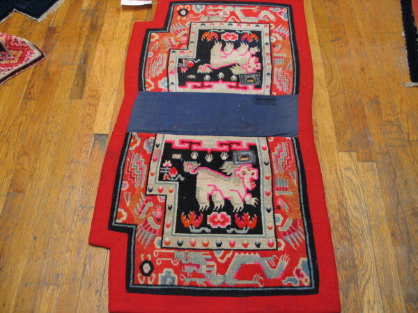 Red and black patterned textile with light mythical animals and a central blue band, displayed on wood floors.