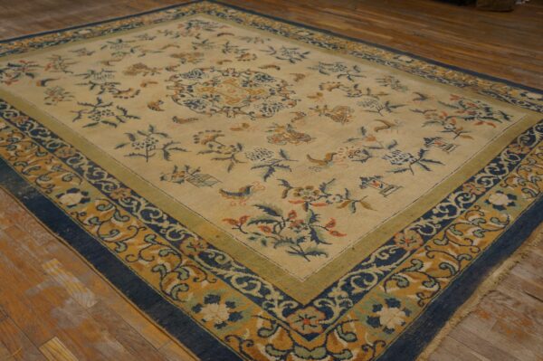 A beige floral rug featuring blue, gold, and green borders is displayed on rustic wooden floorboards.