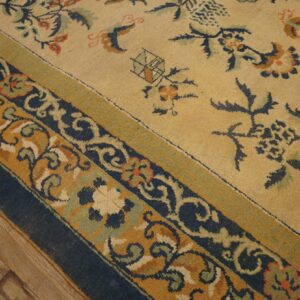 Pale yellow field rug with navy, mustard, and sage green scrollwork borders over wood planks.