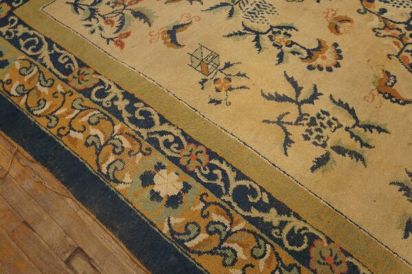 Pale yellow field rug with navy, mustard, and sage green scrollwork borders over wood planks.