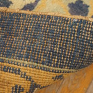 Close-up of a rug's tightly woven blue and tan backing curling over aged orange wood planks.