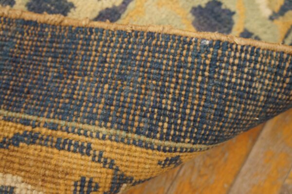 Close-up of a rug's tightly woven blue and tan backing curling over aged orange wood planks.