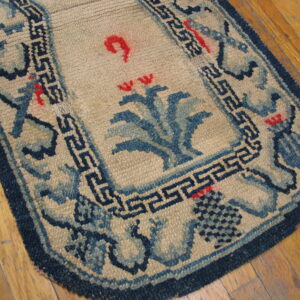 Tan low-pile rug with navy blue fretwork borders and central blue and red floral motifs on wood flooring.