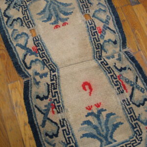 Worn beige runner with blue and red motifs, showing wood flooring through holes in the low pile.