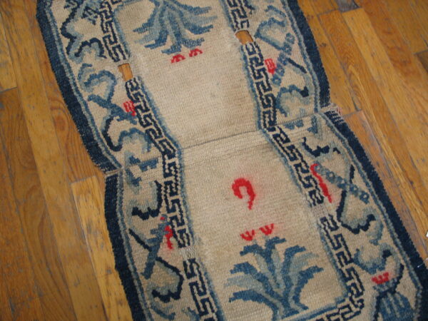 Worn beige runner with blue and red motifs, showing wood flooring through holes in the low pile.