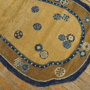 Tan shaped rug with blue circular patterns and a brown-and-blue scalloped border lying on wood planks.