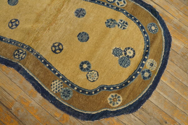 Tan shaped rug with blue circular patterns and a brown-and-blue scalloped border lying on wood planks.